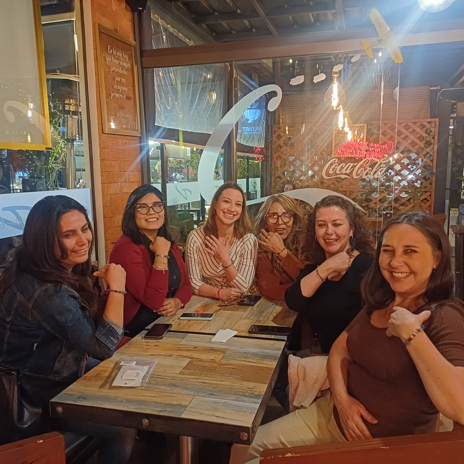 Six women from the Fresh Hope Bolivia group smiling around a table and showing the bracelets on their wrists